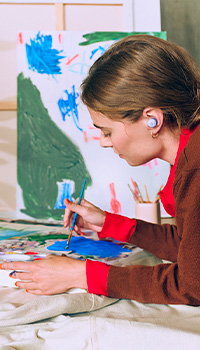 Picture of a woman painting while wearing the Pixel Buds 2a in Iris colour