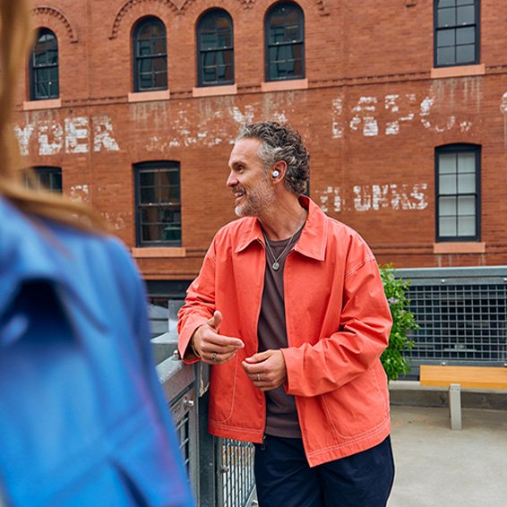 Picture of a man wearing a coral jacket outside wearing Pixel Buds 2a in Iris colour