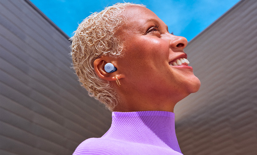 Close-up picture of a woman smiling and looking up to the sky wearing Pixel Buds 2a in Iris colour