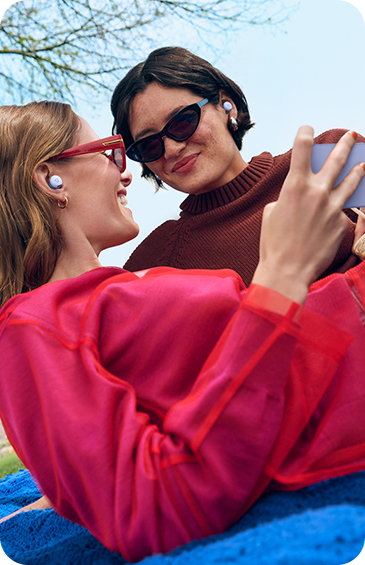 Picture of two women taking a selfie, wearing sunglasses and smiling with Pixel Buds 2a in their ears