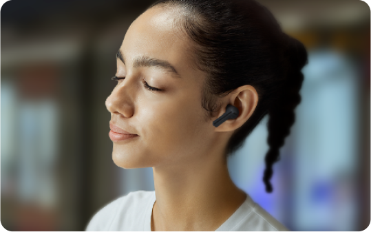 A woman on a train platform with her eyes closed, wearing Buds3 FE to block out the sounds around her