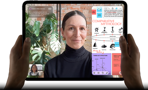 iPad Pro, front exterior, landscape orientation, space black colour, rounded corners, black display bezel, hands holding left and right sides, display showing a FaceTime conversation being live translated, and an educational app showing a presentation of Comparative Mythology with text, diagrams and handwritten notes